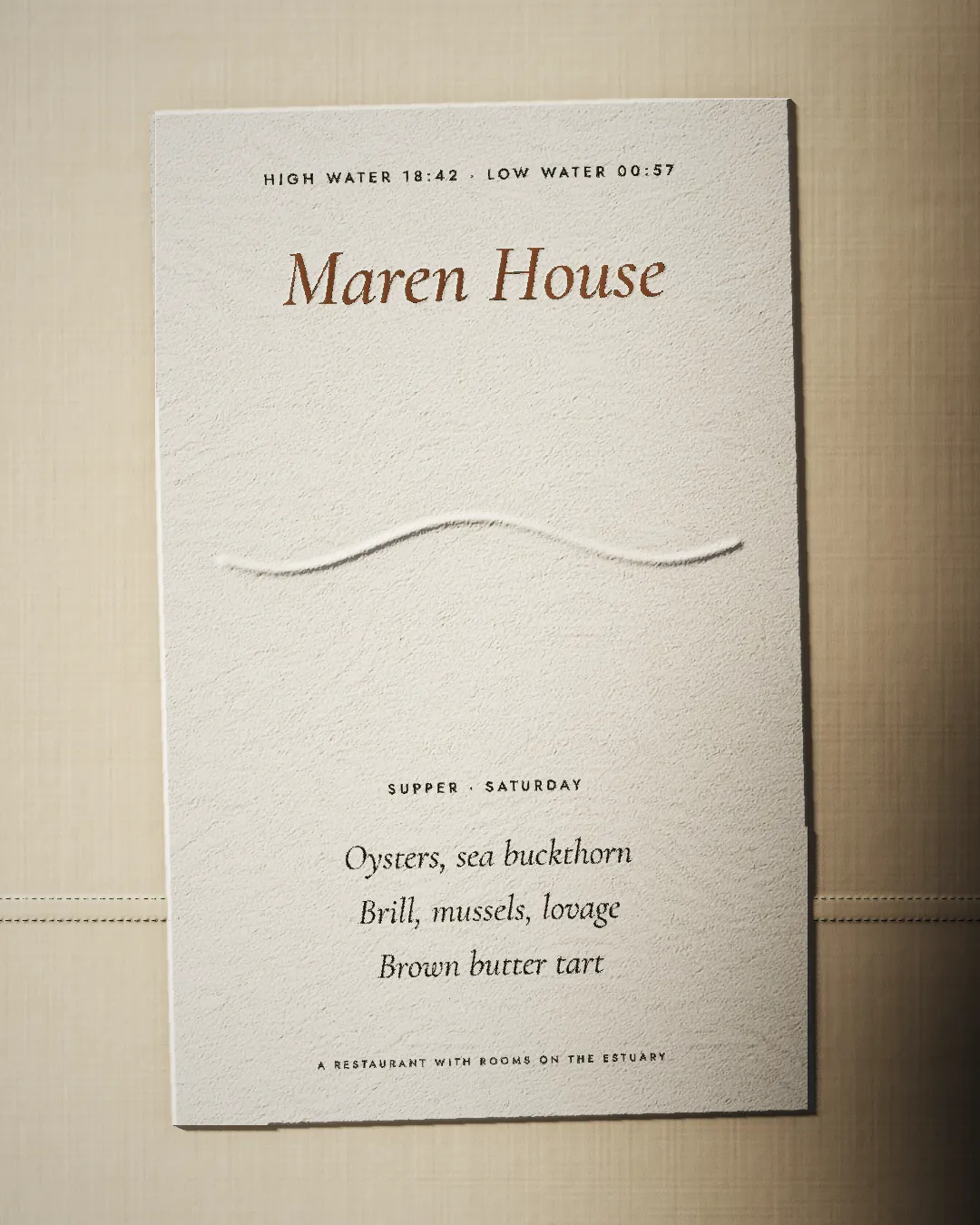 The menu card on linen: tide times along the top, Maren House in copper foil, an embossed tide line and three dishes.