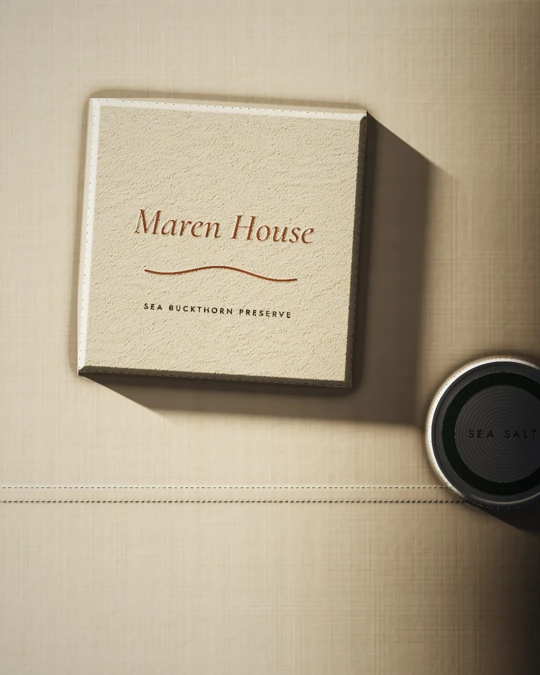 A sea buckthorn preserve box with the name and tide line in copper foil, beside a sea salt tin.